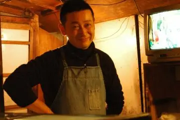 <p>คุณลุงเจ้าของร้าน ด้านบนมีป้ายรายการอาหาร</p>