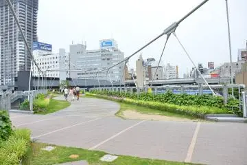 <p>สะพานข้ามไปอีกฝั่งที่รายล้อมไปด้วยสีเขียวของพุ่มไม้และดอกไม้</p>