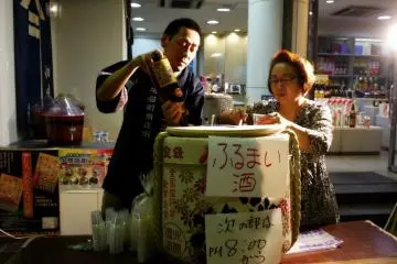 คนคู่นี้กำลังแจกเหล้าสาเกให้ดื่มฟรี แต่ตอนหยุดแจกเพื่อเติมสาเกเพิ่มในถัง