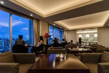 <p>There are a number of different ways to relax at the club lounge. You can sit next to the window and enjoy the sights, or just sit back and relax in one of the many well cushioned chairs in the room. In the background of this photo you can see the room where food is served.</p>