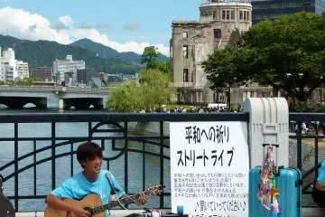 <p>Sur l'un des ponts menant au mus&eacute;e, un artiste joue devant le d&ocirc;me de la bombe atomique</p>