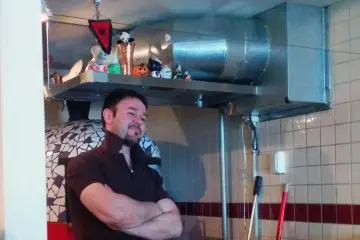 <p>The pizza chef stands proudly in front of his kitchen.&nbsp;</p>