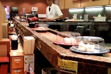 <p>Plates of sushi go around and around in front of you. But you can directly tell the chef what you'd like to eat, then he will make it and hand it to you from inside the counter &nbsp;</p>