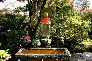 <p>Three o-jizo stand over a water basin</p>