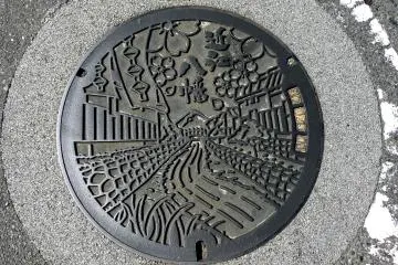 오미하치만의 맨홀 뚜껑은 벚꽃 아래 흐르는 운하를 보여준다.