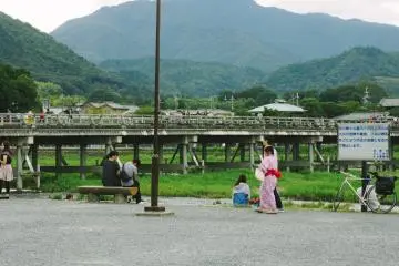 Al pasar por el río Katsura, los turistas se relajan y disfrutan de la tarde de verano. Togetsukyo, al fondo, es uno de los puentes famosos de Arashimaya