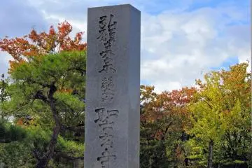<p>Tiang batu penanda Kuil Shougenji yang berdiri tegak dengan latar warna dedaunan musim gugur</p>