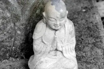 <p>A small Jizo statue sitting silently at the foot of one of the Kannon Bosatsu statues</p>