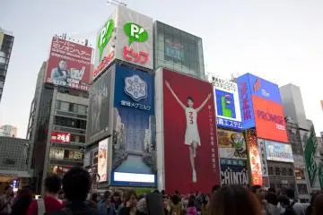 <p>Glico Girl >>> และนี่คือป้ายชั่วคราวอันที่สองซึ่งยังคงเป็น&nbsp;อายาเซะ ฮารูกะ (Ayase Haruka) คนเดิมที่ใส่ชุดกูลิโกะสีขาวชูมืออยู่บนป้ายพื้นสีแดงสด พร้อมข้อความที่ว่า 新しいグリコの看板、完成間近！ที่แปลได้ว่า &ldquo;ป้ายไฟกูลิโกะอันใหม่ ใกล้เสร็จสมบูรณ์แล้ว!&rdquo;</p>