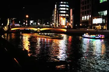 <p>Lit-up cruise boat gliding on Tosabori River under Tenjinbashi Bridge</p>