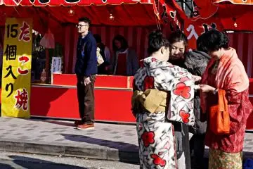 <p>Women dressed in kimono sharing a snack from one of the food stalls</p>