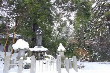 <p>Temple grounds buried in snow with the statue of the monk Taicho flanked by stone lanterns</p>