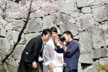 <p>เจ้าสาวและเจ้าบ่าวหยุดมองรูปถ่ายของพวกเขาภายใต้ต้นซากุระ</p>