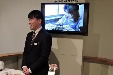 <p>Friendly assistant stands next to an audio-visual of the culturing process</p>
