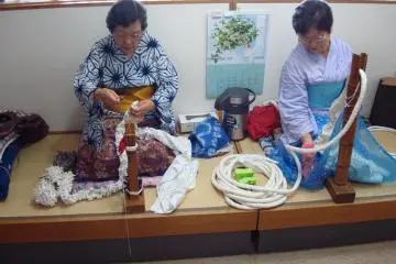 Ladies demonstrate different shibori techniques.  They are both wearing clothes in the pattern they are creating.