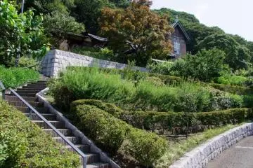 Rumah ini terletak persis di belakang taman. Naiki tangga di sebelah kiri, atau jalan landai di sebelah kanan.