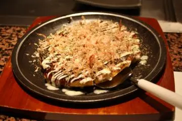 <p>A bit of hanakatsuo (pieces of katsuobushi, also called the dancing fish) on it when it is still hot: it looks like it is truly dancing on the Okonomiyaki</p>