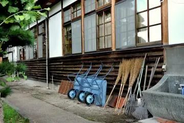 Wheelbarrows and brooms lean against a building's side