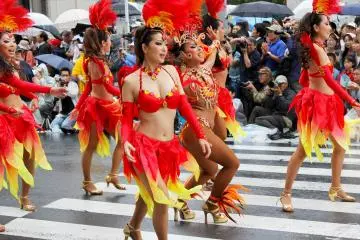 The dancers have various color coordinated outfits with one samba outfit dancer surrounded by costumed dancers.&nbsp;