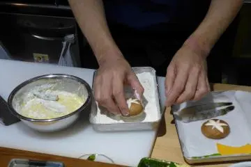The chef demonstrates how to coat the tempura ingredients before cooking.