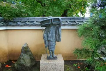 A statue at the entrance and maple trees in the background