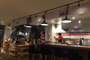 A customer sitting at the bar while the staff prepare food.