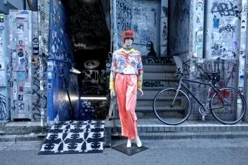 A lone mannikin stands eccentrically dressed at the entrance to a mysterious basement