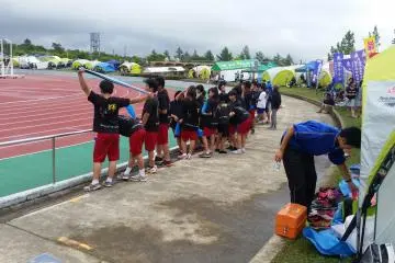 Young athletes watch runners amid a busy group of school tents