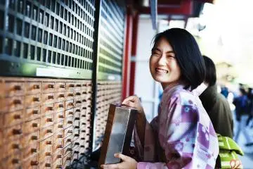 Young girl in traditional dress tries her fortune with omikuji