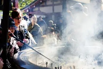 People around incense burner, they take their hands and direct some of the incense smoke over their body