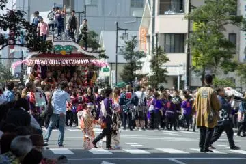Performers cross the street as participants pull their float