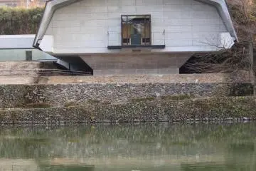 The Hirose Memorial Museum overlooks a large square pond which is surrounded by a walkway and cherry trees.