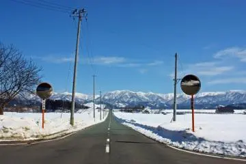 Winter: On a clear day, the surrounding mountains are striking against the sky. This road appears to lead straight towards them.