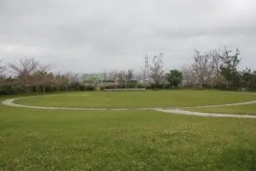 An open air gathering area in the native village area on the grounds of the Zakimi Castle Ruins.  A stage can be seen in front of the grassy viewing area.