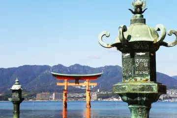 Una linterna de bronze dai-toro con las montañas y el Tori Flotante en el fondo. La linterna en la izquierda se encuentra en realidad entre otras dos linternas. ¿Notaste la diferencia en los ornamentos metálicos sobre cada linterna?