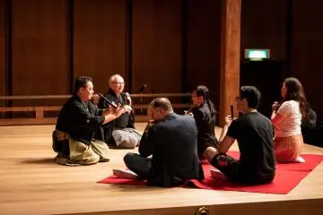 นักดนตรีโนะอธิบายอาสาสมัครถึงวิธีการเล่นฟุเอะหรือขลุ่ย