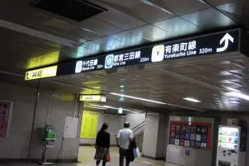 Commuters pass the green payphone and vending machine. The illumated red display features various destinations in the area.