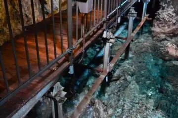 Water rapids flow under the visitor's path inside the cave.