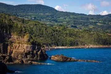 Rocky, forested coastline with mountains and windmills surround the shrine