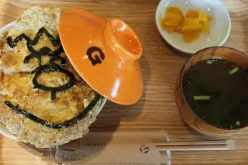<p>อาหารที่เสิร์ฟในคาเฟ่ของพิพิธภัณฑ์ล้วนมีความหมาย นี่คือทงคัตสึ ด้ง(หมูทอดวางบนข้าว) พร้อมโนริ (สาหร่าย) ออกแบบให้เหมือนไจแอนท์</p>