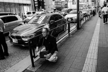A Japanese middle-aged man squats down by the sidewalk and take a smoke break.