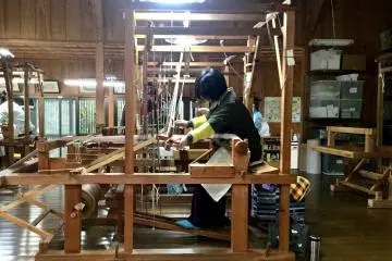A weaver at the tall loom producing centuries-old traditional fabric