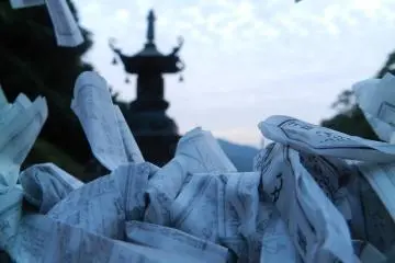 Fortunes tied to a fence with a pagoda against the evening sky.