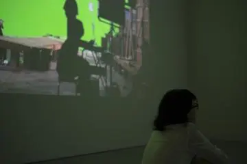 A woman watches the main film while the making of is projected just to her left