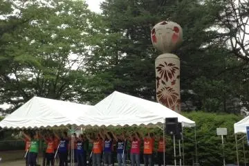A children's gospel choir sings in front of a large Kokeshi Doll in Nishikoen Park.