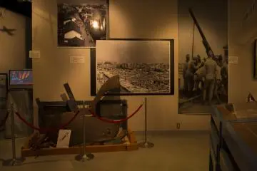 The remnants of an exploded shell stand in front of a photograph that depicts Osaka in complete ruins