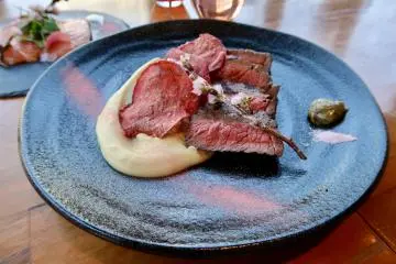 A platter of grilled steak, potato puree, beet chips, cherry blossom leaf and rhubarb jam, and cherry blossom salt