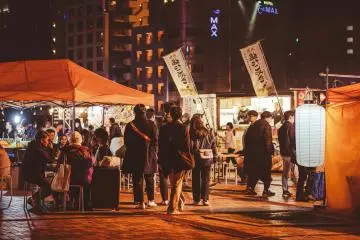 Fukuoka's yatai provide both delicious food and a unique cultural experience (Photo: <a href="https://unsplash.com/photos/a-group-of-people-standing-around-a-food-stand-at-night-wj5QuDIuZBI" target="_blank" rel="noreferrer noopener nofollow">Tracy Xu</a> / Unsplash)
