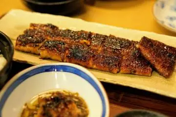 Slices of grilled unagi, surrounded by more dishes