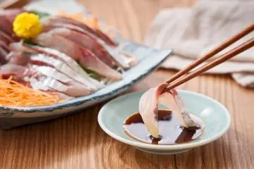Mackerel sashimi being dipped into soy sauce